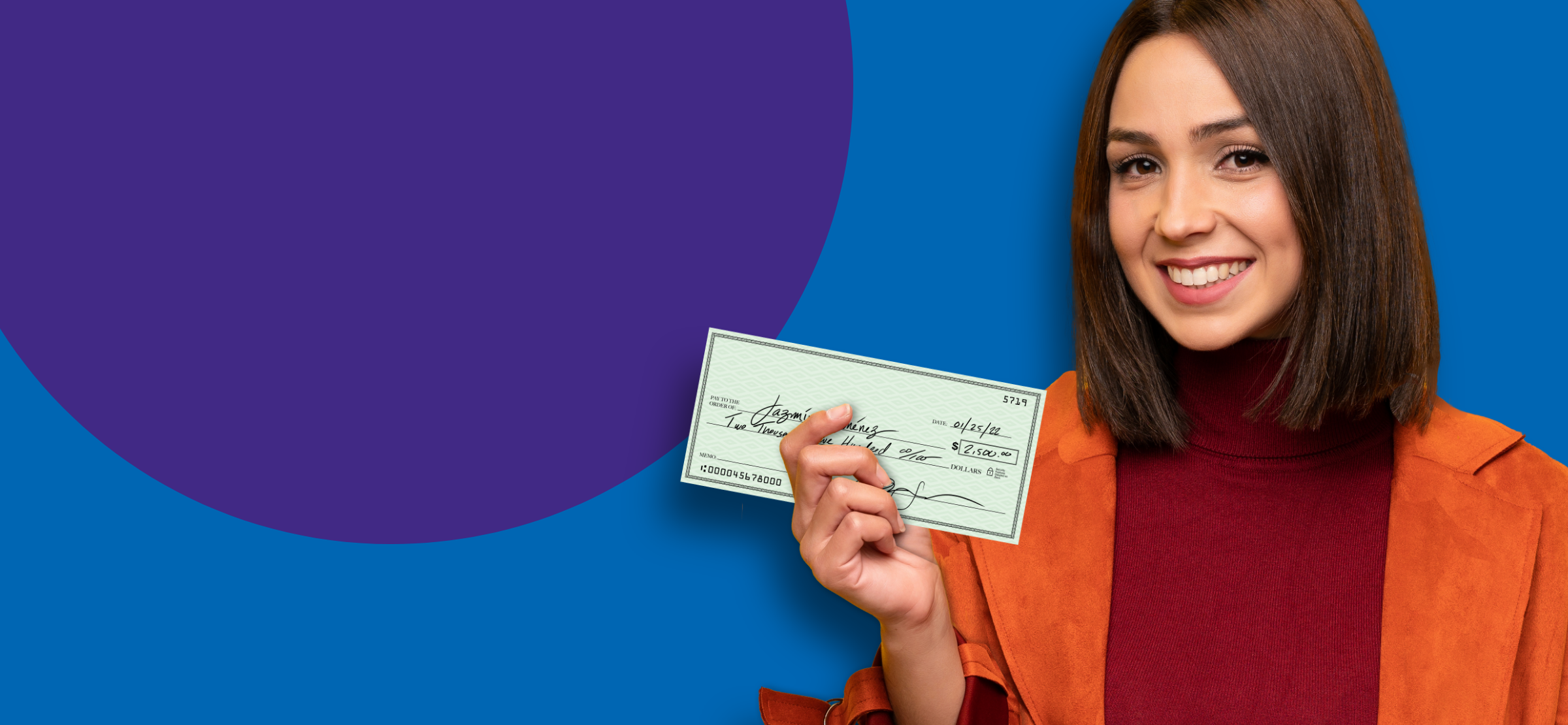 A woman in an orange coat smiling, holding a cheque.