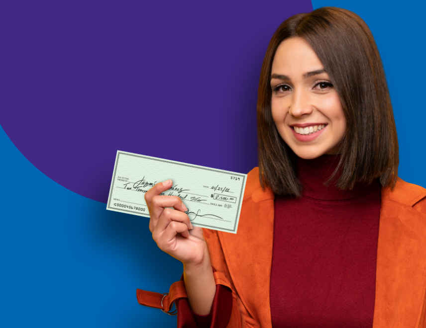 A woman in an orange coat smiling, holding a cheque.